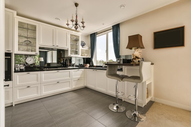 a kitchen with white cabinets and black counter tops on the island in front of the bar stools that is next to the sink