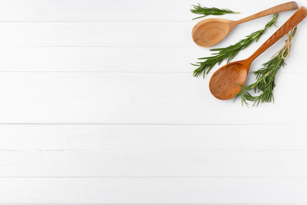 Kitchen wooden spoon with rosemary on white wooden background