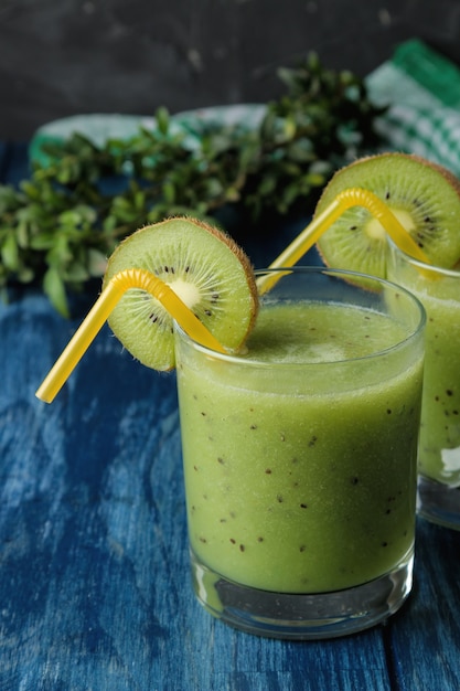 Kiwi smoothies in a glass next to fresh kiwi slices on a blue wooden table. fruit drink.