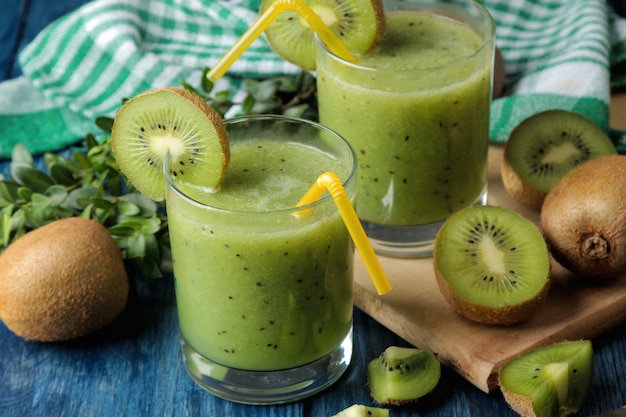 Kiwi smoothies in a glass next to fresh kiwi slices on a blue wooden table. fruit drink.