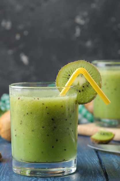 Kiwi smoothies in a glass next to fresh kiwi slices on a blue wooden table. fruit drink.