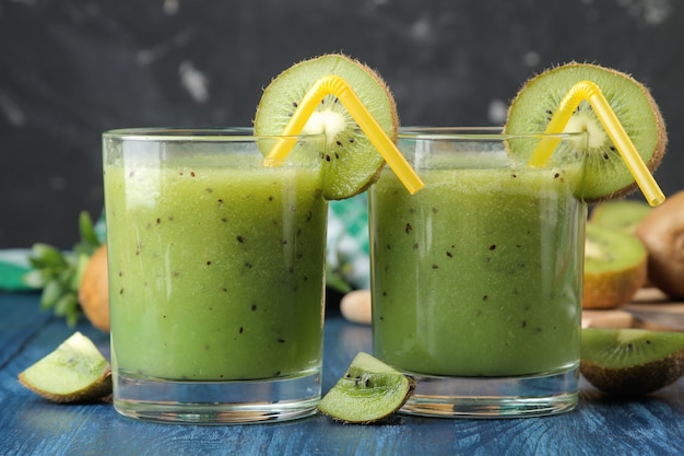 Kiwi smoothies in a glass next to fresh kiwi slices on a blue wooden table. fruit drink.