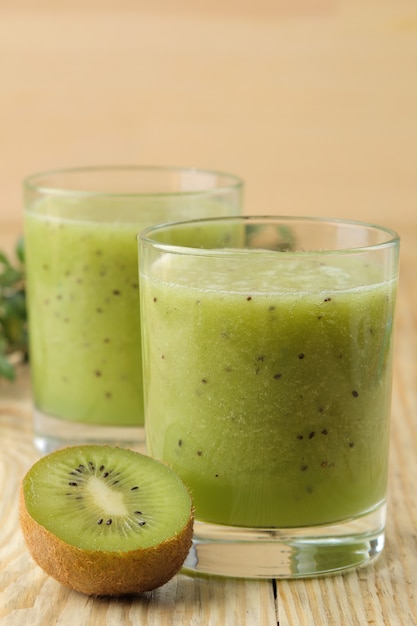 Kiwi smoothies in a glass next to fresh kiwi slices on a natural wooden table.