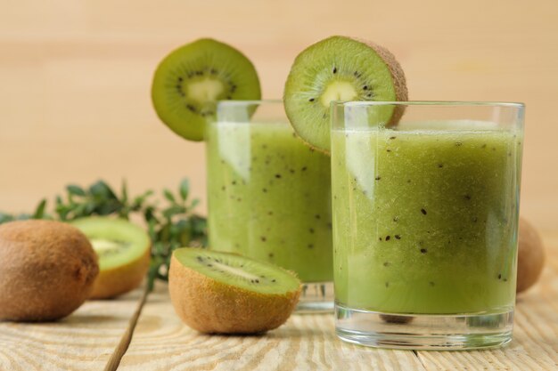 Kiwi smoothies in a glass next to fresh kiwi slices on a natural wooden table.