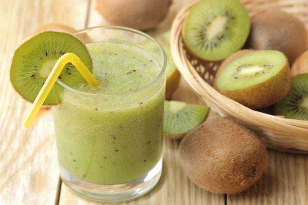 Kiwi smoothies in a glass next to fresh kiwi slices on a natural wooden table.