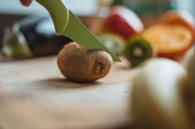 A kiwifruit being cut on a wooden table surrounded by other fruits.