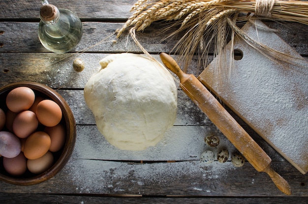 Kneaded dough, ears of wheat,rolling pin, eggs and a bottle of oil on the old rustic table closeup