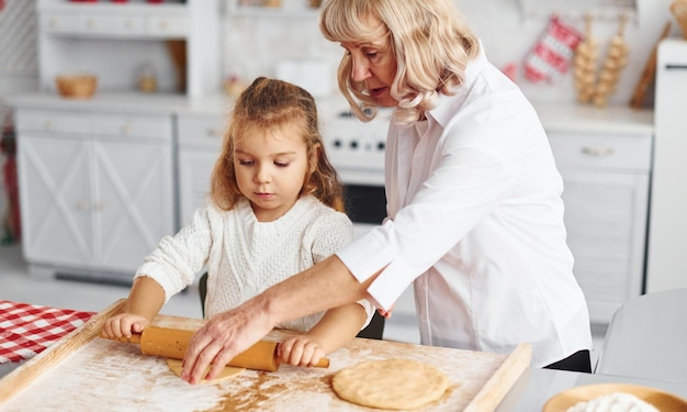 Kneads the dough Senior grandmother with her little granddaughter cooks sweets for Christmas on the kitchen