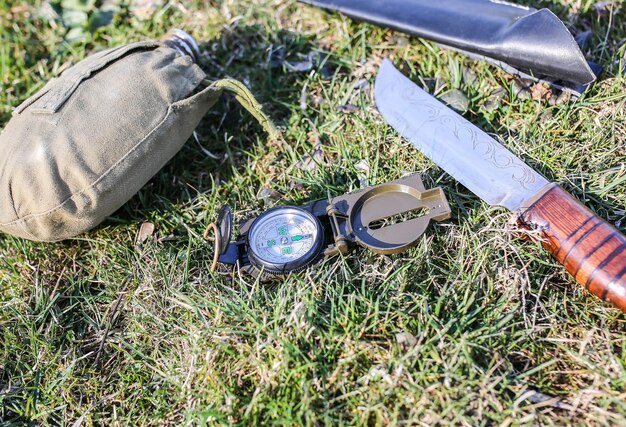 Photo knife, compass and flask lying on the grass. tourist things for hiking in the nature. old vintage style.