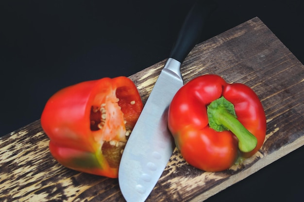 Knife cutting red pepper on wooden board