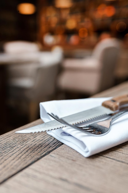 A knife and fork sit on a napkin on a table in a restaurant.