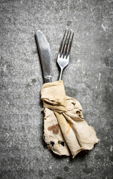 Knife and fork wrapped in old cloth. On a stone background.