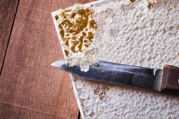 Knife on honeycomb with honey on a wooden background.