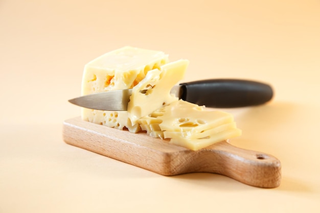 The knife is cutting a piece of cheese with holes on a wooden board