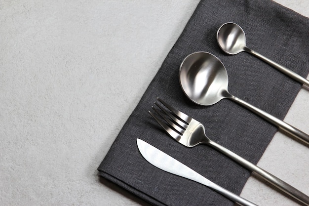 Knife spoons and fork with dark textile napkin on grey stone background Table setting