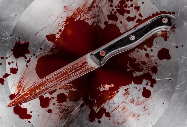 Photo a knife with a red handle is on a silver plate with blood on it.