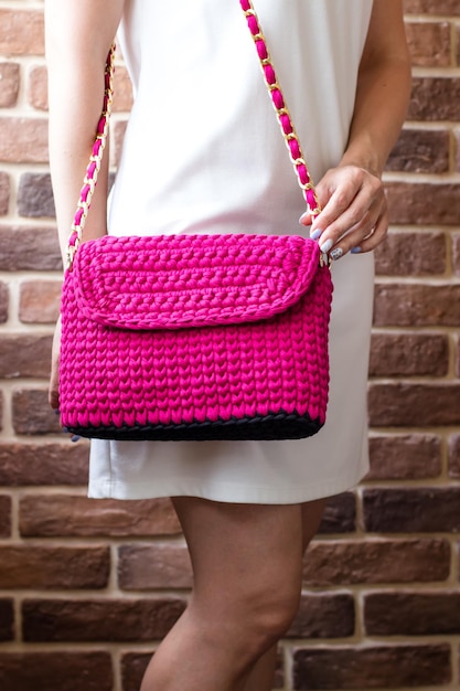 Knitted bag on a girl in a white dress against a brick wall