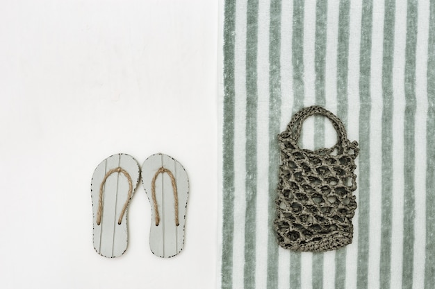 Knitted beach bag and grey flip-flops on white with copy space. Beach towel striped pattern. Concept of beach holiday.