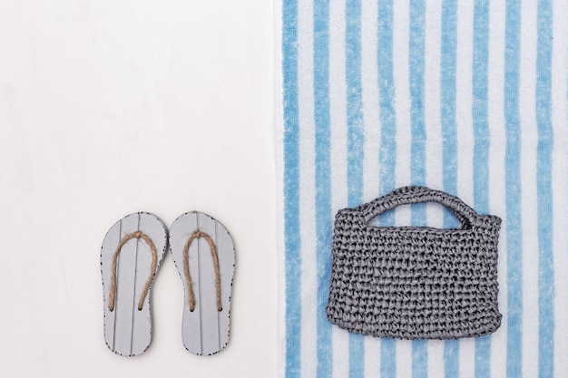 Knitted beach bag and grey flipflops on white background with copy space Beach towel striped pattern