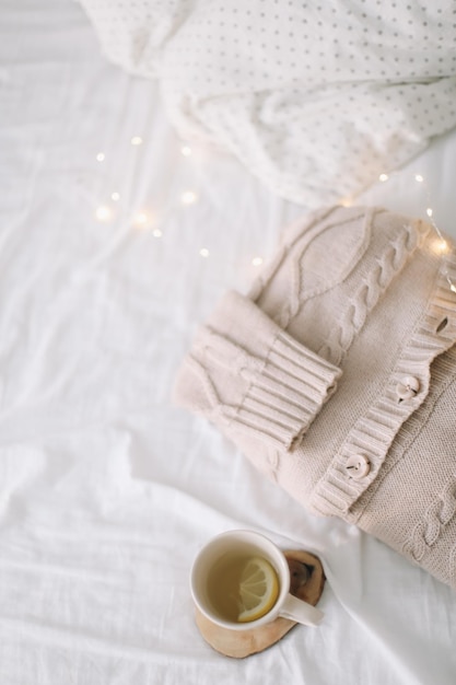 Knitted beige sweater and cup of tea on messy bed background winter and spring fashion concept top v...