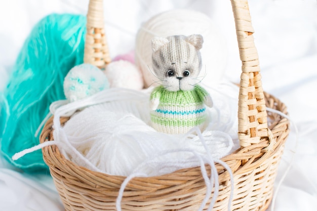 A knitted kitten with knitting needles colored balls of thread in a basket Creative workshop on needlework handmade