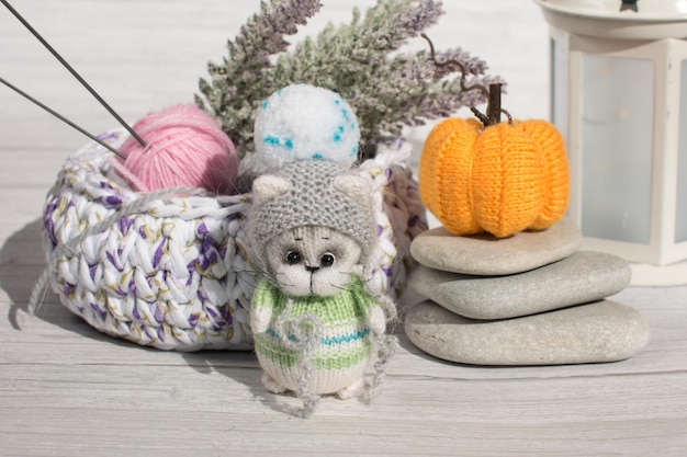 A knitted kitten with knitting needles and orange pumpkins colored balls of thread in a basket Creative workshop on handmade needlework