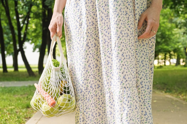 Knitted mesh bag with vegetables and fruits in the hands of a woman