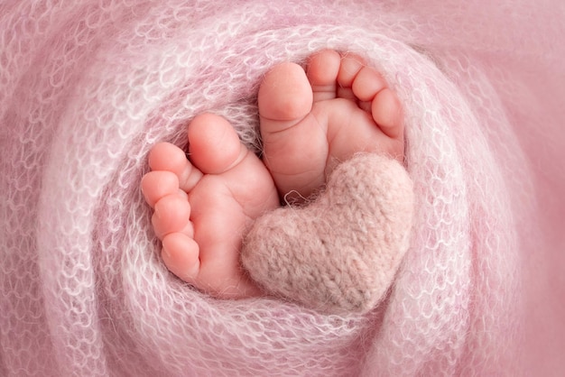 Knitted pink heart in the legs of a baby Soft feet of a new born in a pink wool blanket Closeup of toes heels and feet of a newborn Macro photography the tiny foot of a newborn baby