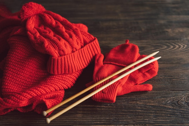 Knitted red hat scarf knitted mittens and wooden knitting needles on wooden background Hobby craft Concept of knitting needlework