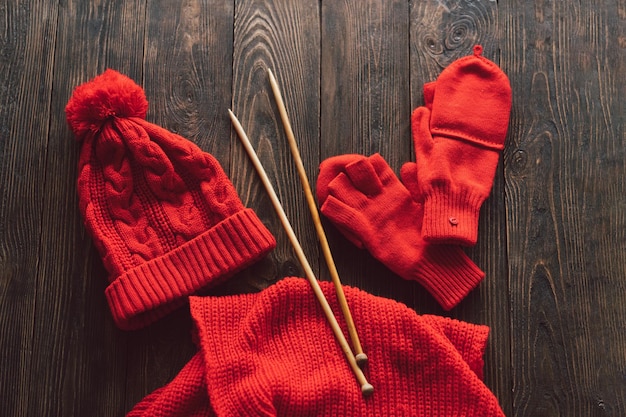 Knitted red hat scarf knitted mittens and wooden knitting needles on wooden background Hobby craft Concept of knitting needlework