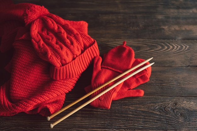 Knitted red hat scarf knitted mittens and wooden knitting needles on wooden background Hobby craft Concept of knitting needlework