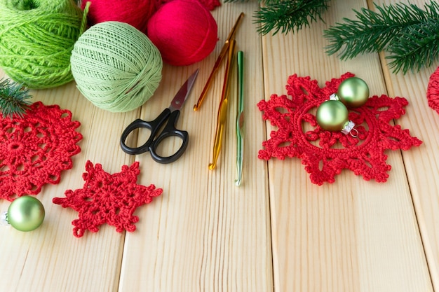 Knitted red snowflakes, threads and hooks on wooden background.