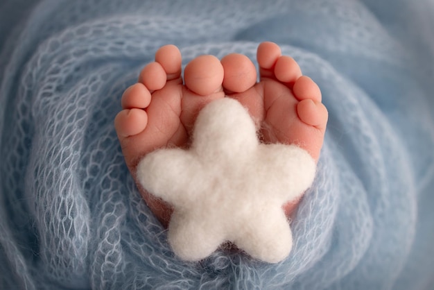 Knitted white star in the legs of a baby Soft feet of a new born in a blue wool blanket Closeup of toes heels and feet of a newborn Macro photography the tiny foot of a newborn baby