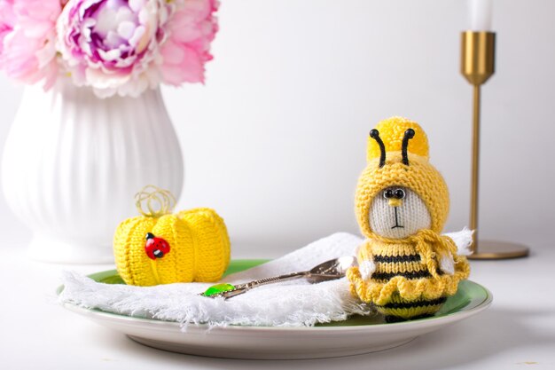 A knitted yellow bee sits on a white plate with a daisy Handmade knitting toy amigurumi gift for Children