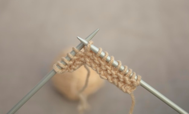 Knitting on metal needles with beige yarn. Hobby and needlework concept.