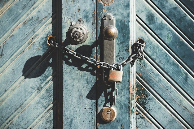 Knob and padlock on a weathered blue wooden door of an old factory