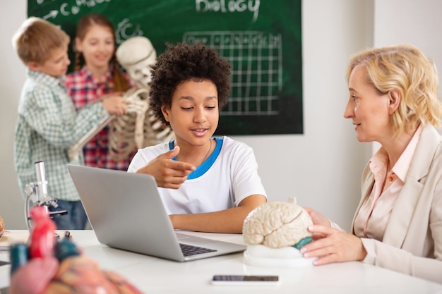 Knowledge control. Smart nice boy pointing at the human brain while telling his teacher about it