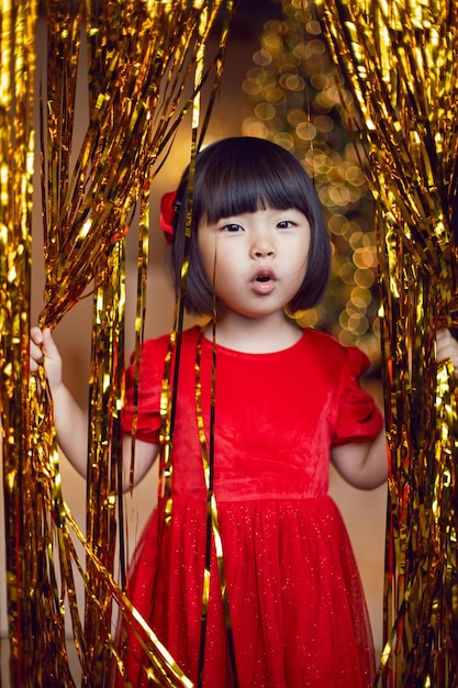 Korean girl child in red dress is playing on Christmas night with golden tinsel