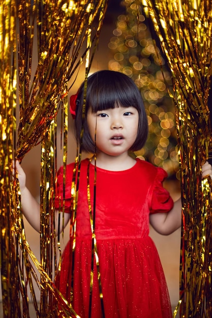 Korean girl child in red dress is playing on Christmas night with golden tinsel