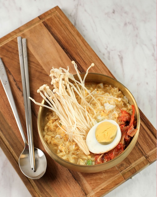 Korean Ramyeon on Gold Bowl, Serve with Shimeji Mushroom, Kimchi, and Half Boiled Egg on White Marble Table, Top View