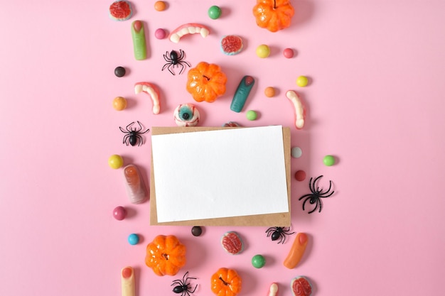 Kraft envelope with empty paper on the background of various sweets on a pink background Happy Halloween A place to copy Flat position top view