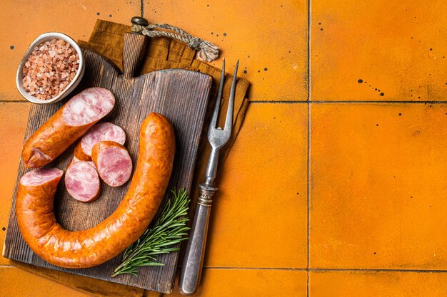 Photo krakow smoked sausage with rosemary and spices on a wooden board orange background top view copy space