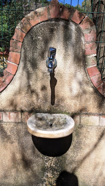 Kuosk of a decorative wall made of concrete with a builtin metal faucet and a ceramic sink