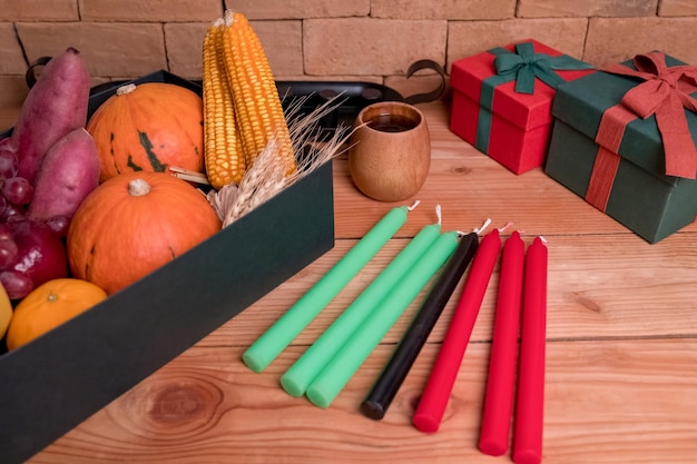 Kwanzaa holiday concept with decorate seven candles red, black and green, gift box, pumpkin,corn and fruit on wooden desk and background.