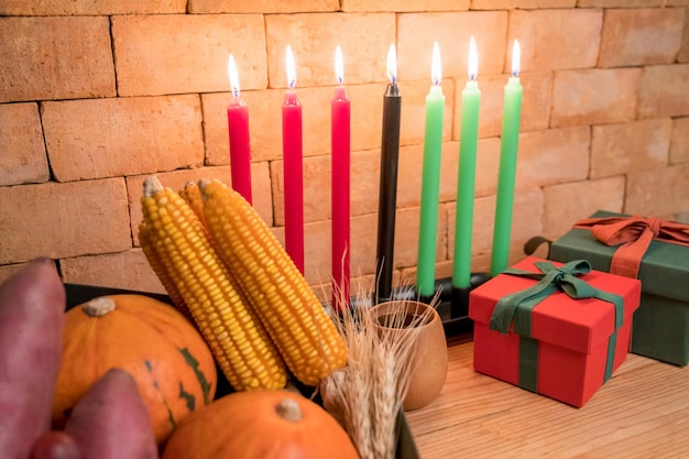 Kwanzaa holiday concept with decorate seven candles red, black and green, gift box, pumpkin,corn and fruit on wooden desk and background.