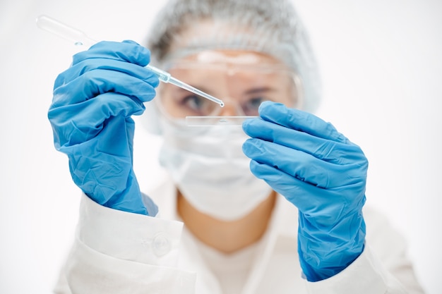 Lab assistant in blue gloves putting reagent onto glass slide with pipette making coronavirus test