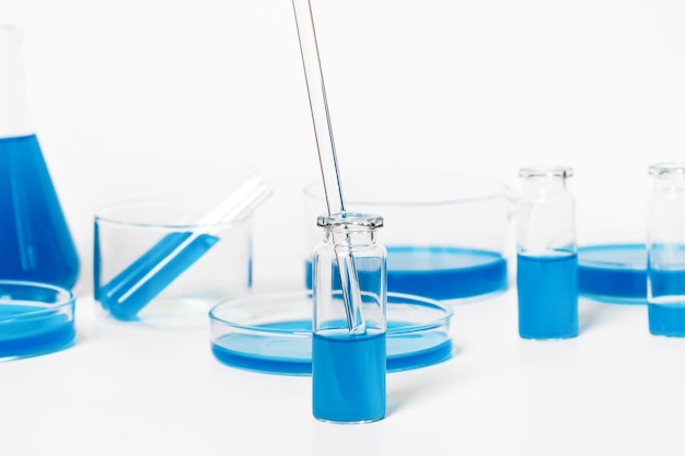 Lab jar with blue blue liquid Pipette glass tube Against the backdrop of laboratory glassware Petri dishes flasks test tubes On a white light background