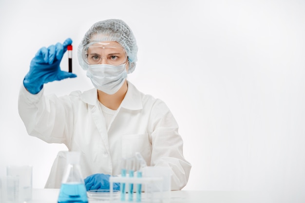 Lab worker in uniform with mask and gloves looking at blood in white background