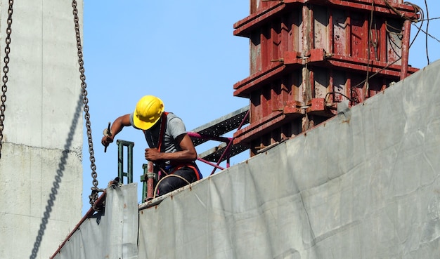 Labor man working on construction site with helmet and safty equipment and covering the building with grey color vinyl and blue sky.