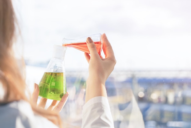 Laboratory assistant standing at the window mixes reagents in flasks in the laboratory at production